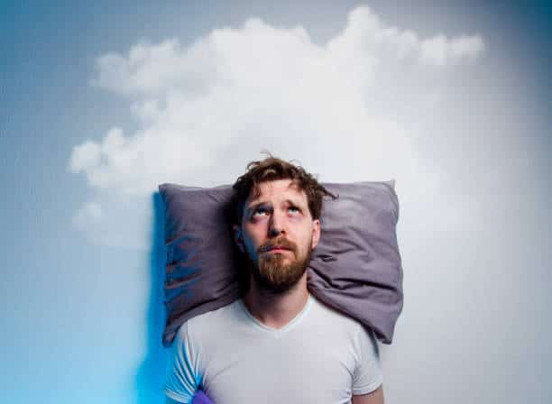 Man having problems/ primary insomnia, laying in bed on pillow, looking up to grey cloud over his head.